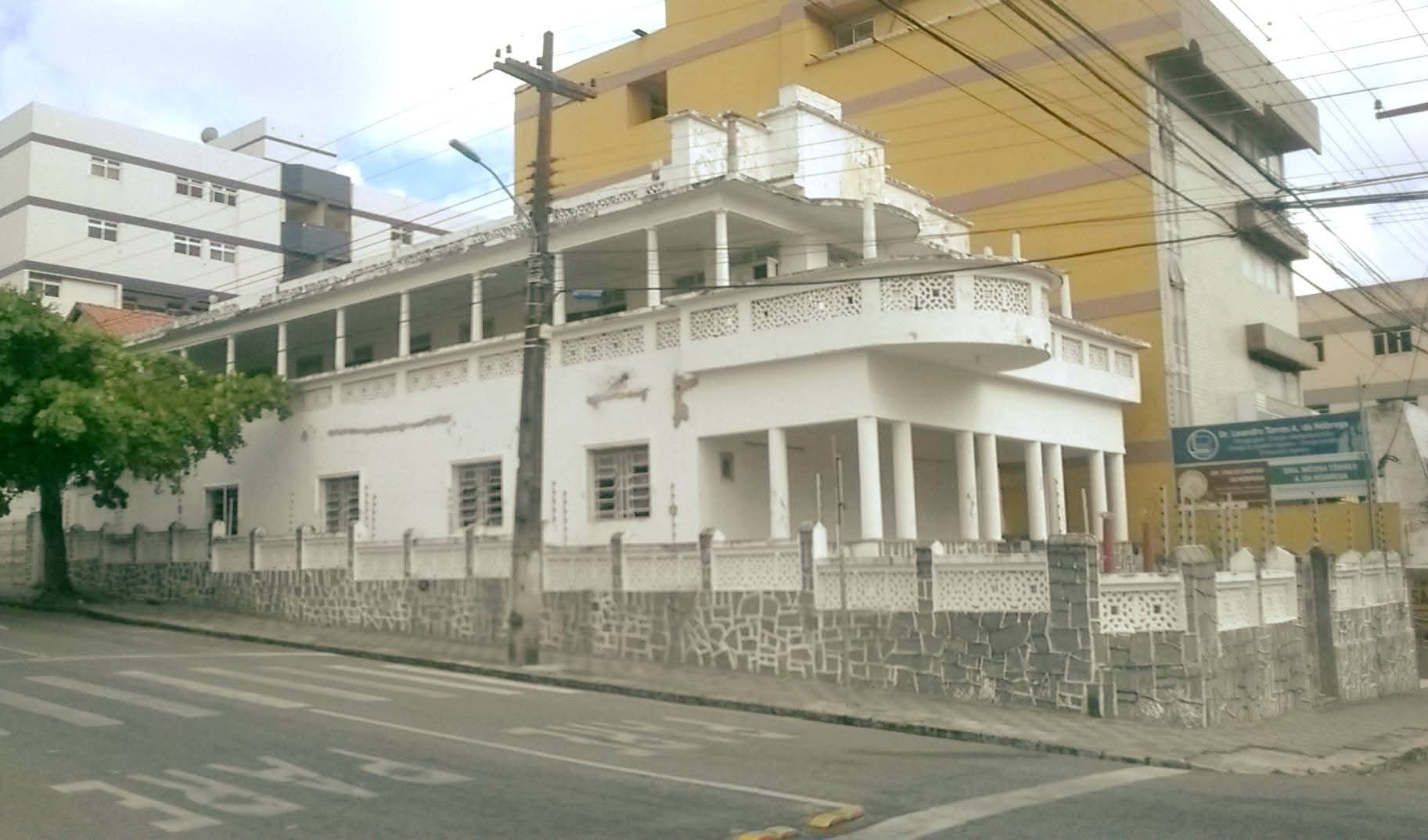 Vista lateral de residência Art Déco em Campina Grande, com varanda curva, cobogós e colunas, mostrando desgaste na pintura.