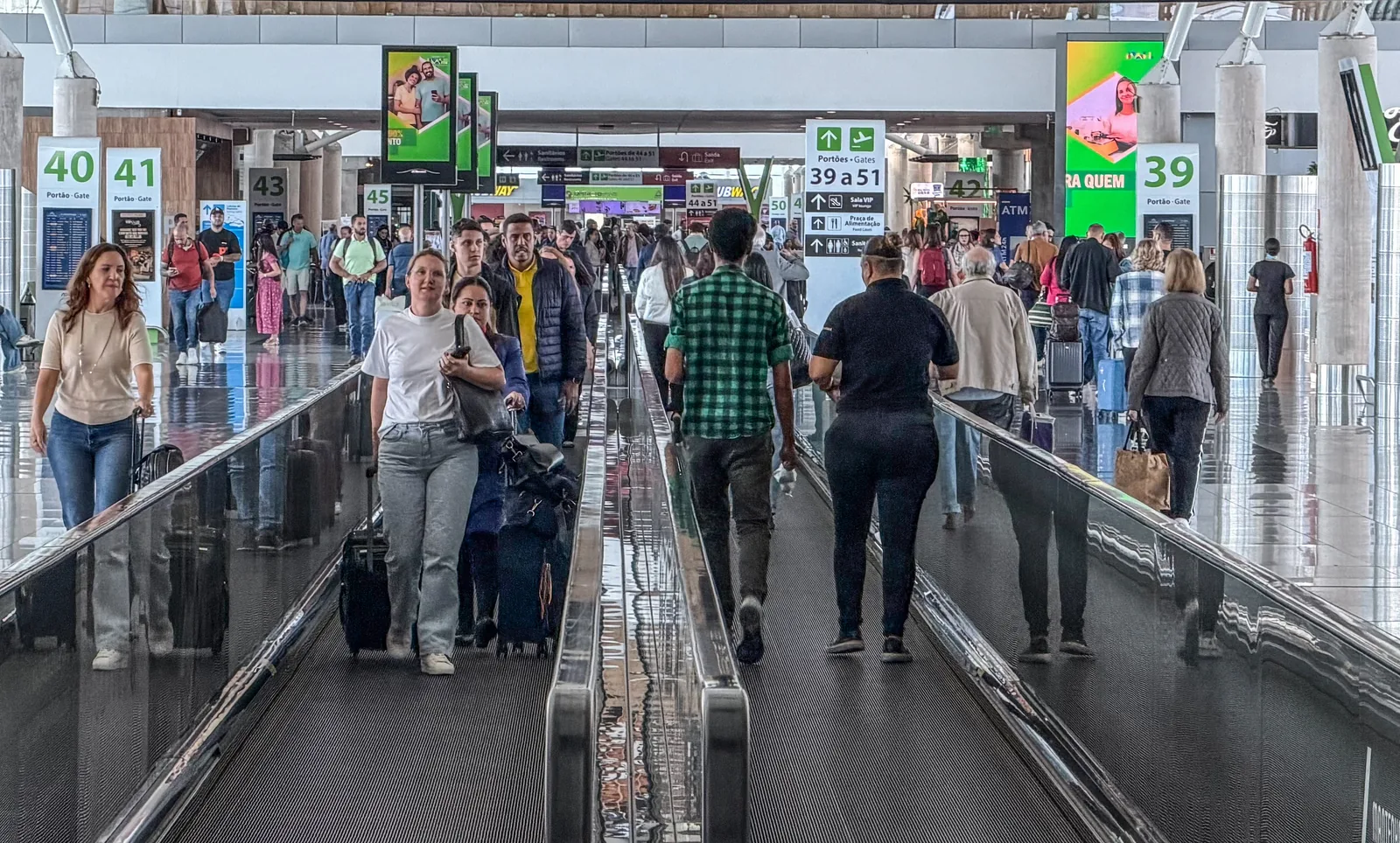 Movimentação de passageiros no Aeroporto de Brasília durante operações de embarque e desembarque, com pessoas circulando pelos terminais com bagagens.