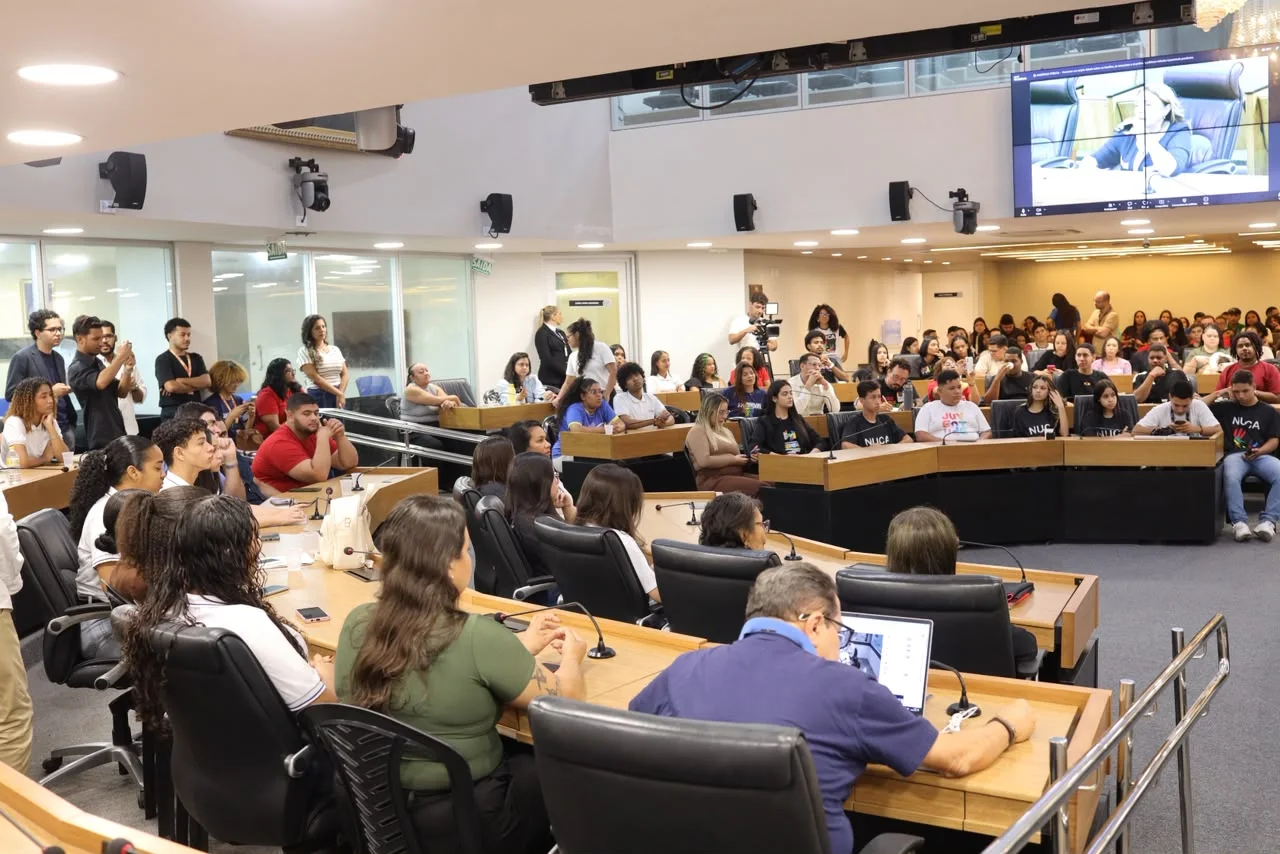 Plenário da Assembleia Legislativa da Paraíba lotado de jovens e participantes durante audiência pública, com telão de transmissão ao fundo.