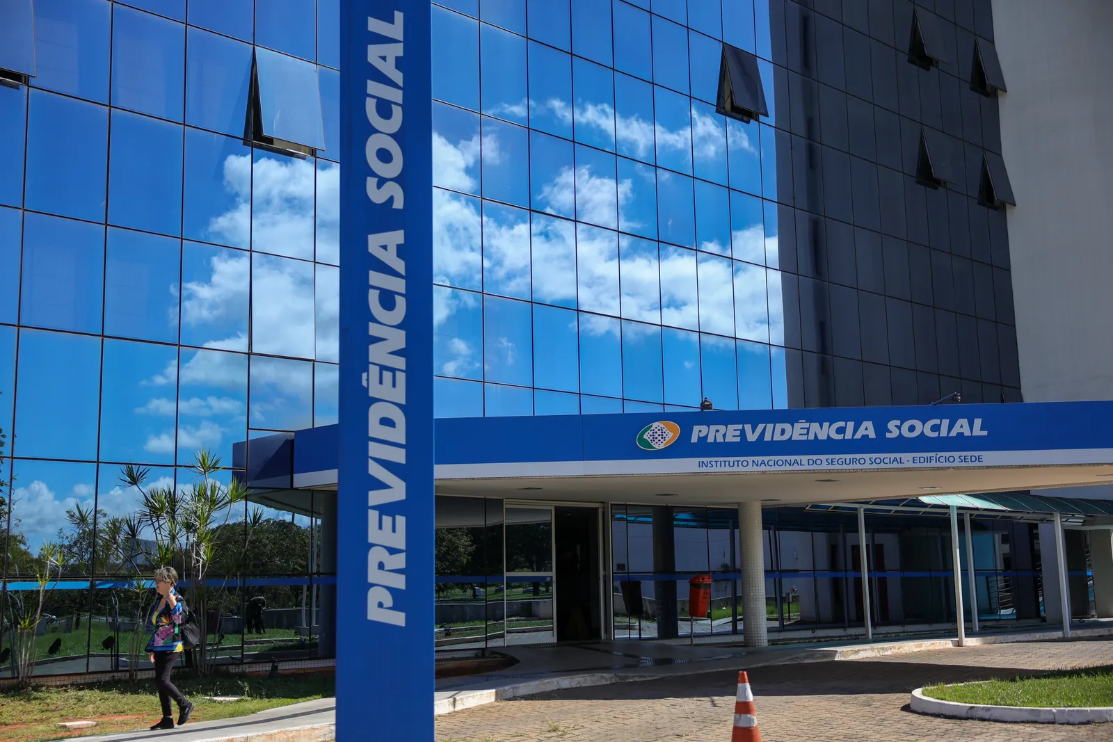 Fachada de vidro azul do edifício sede do INSS, em Brasília, com totem vertical escrito Previdência Social.
