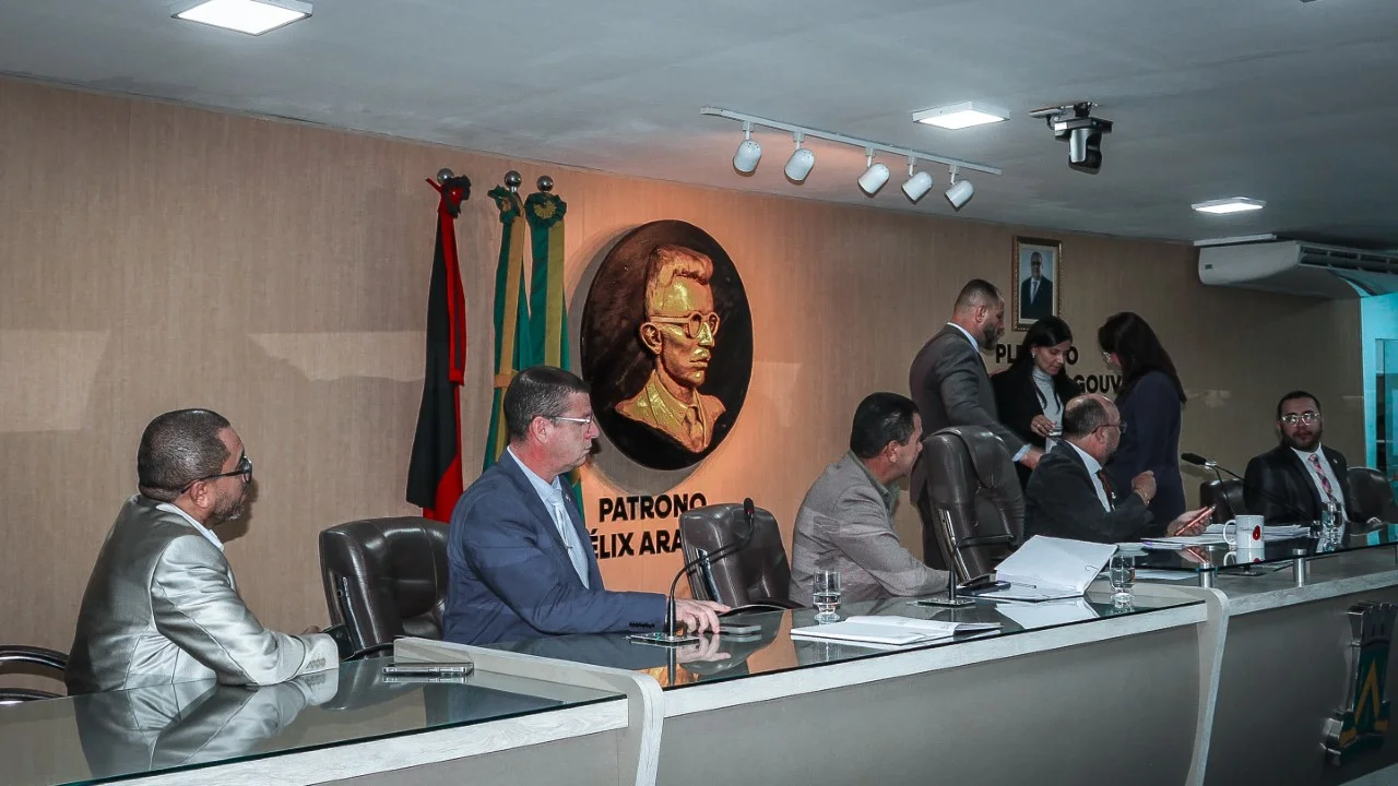 Vereadores sentados na mesa diretora da Câmara Municipal de Campina Grande, com a efígie do patrono Félix Araújo e as bandeiras da Paraíba e do Brasil ao fundo.