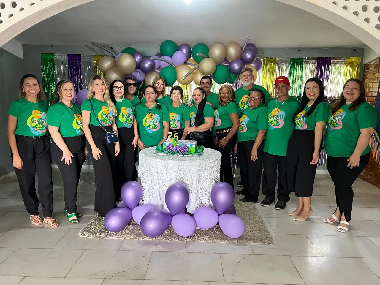 Grupo de participantes e equipe do centro posa ao lado do bolo de 26 anos com balões