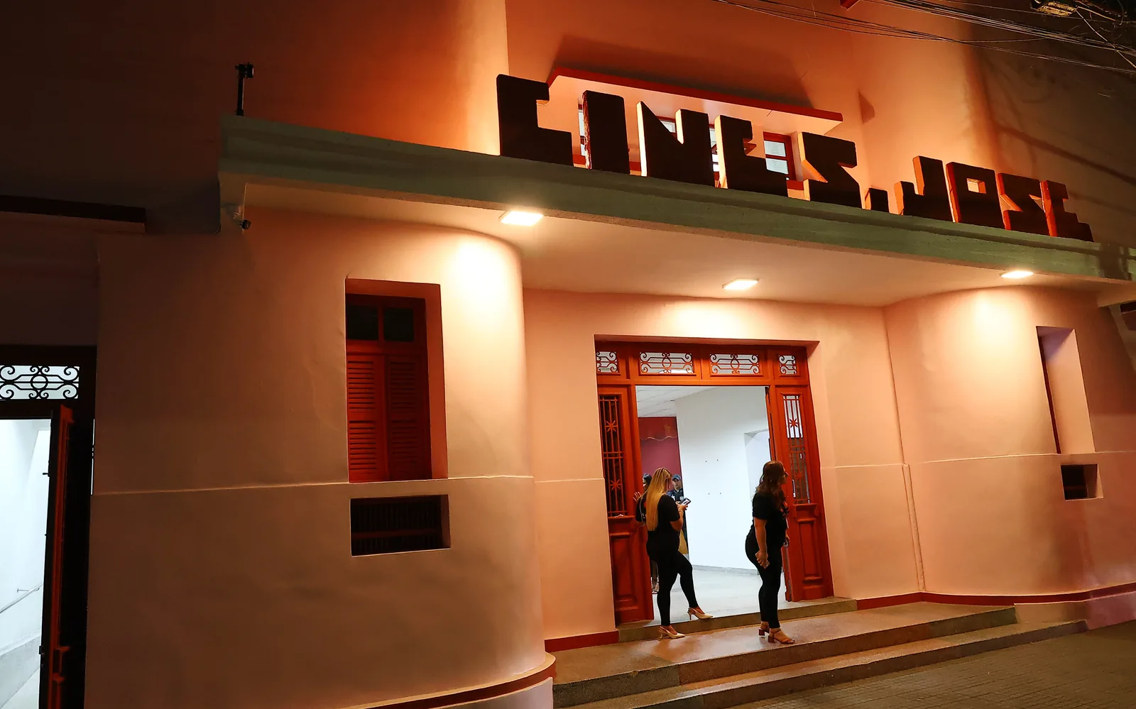Fachada iluminada em estilo art déco do Cineteatro São José à noite, com o letreiro Cine S. José e pessoas na entrada