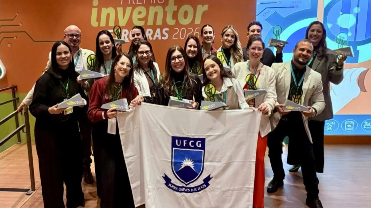 Grupo de pesquisadores segura uma bandeira da UFCG e troféus do Prêmio Inventor Petrobras diante de um painel colorido.