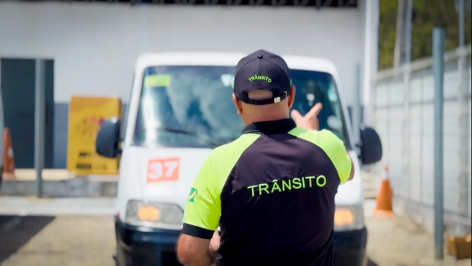 Agente de trânsito da STTP de costas, com colete refletivo escrito Trânsito e boné, orientando um veículo de transporte escolar