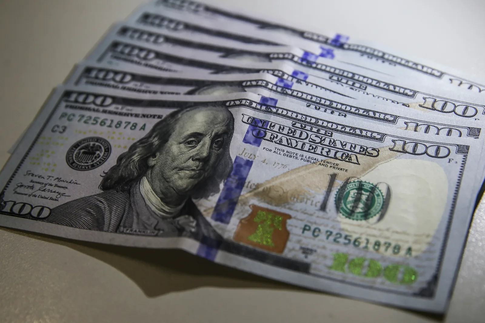 Cédulas de 100 dólares americanos espalhadas lado a lado sobre uma mesa.
