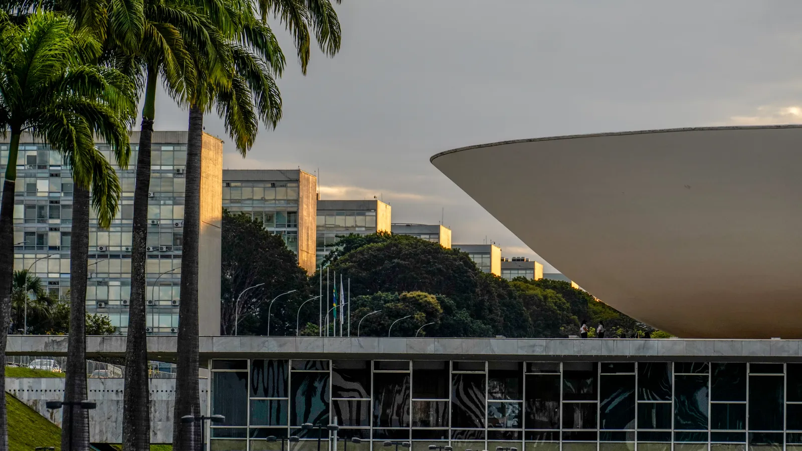 A semiesfera invertida do plenário da Câmara dos Deputados no Congresso Nacional, ao entardecer, com palmeiras e prédios dos ministérios ao fundo.