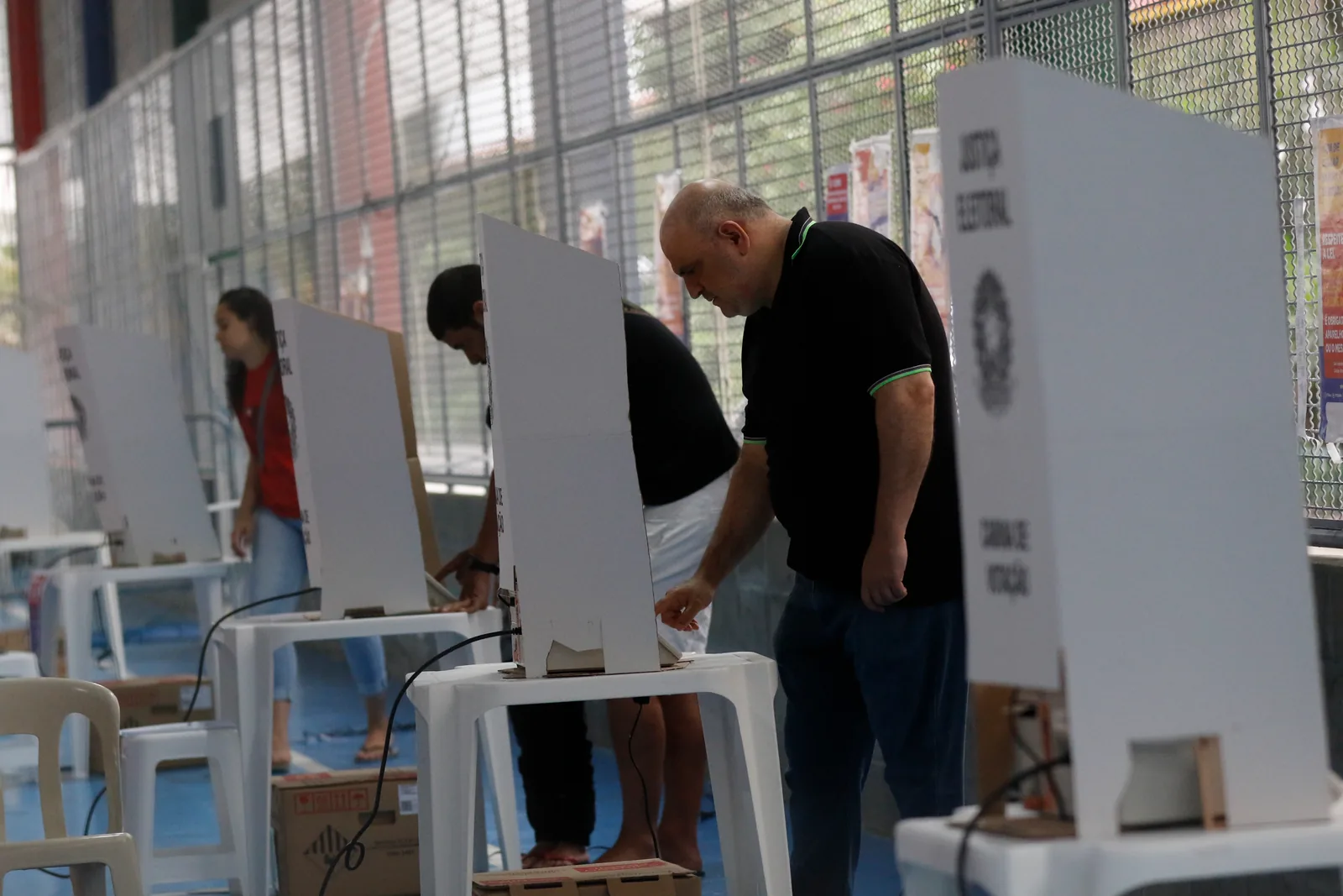 Eleitores votam em seção eleitoral, diante de urnas eletrônicas, durante votação no Brasil.