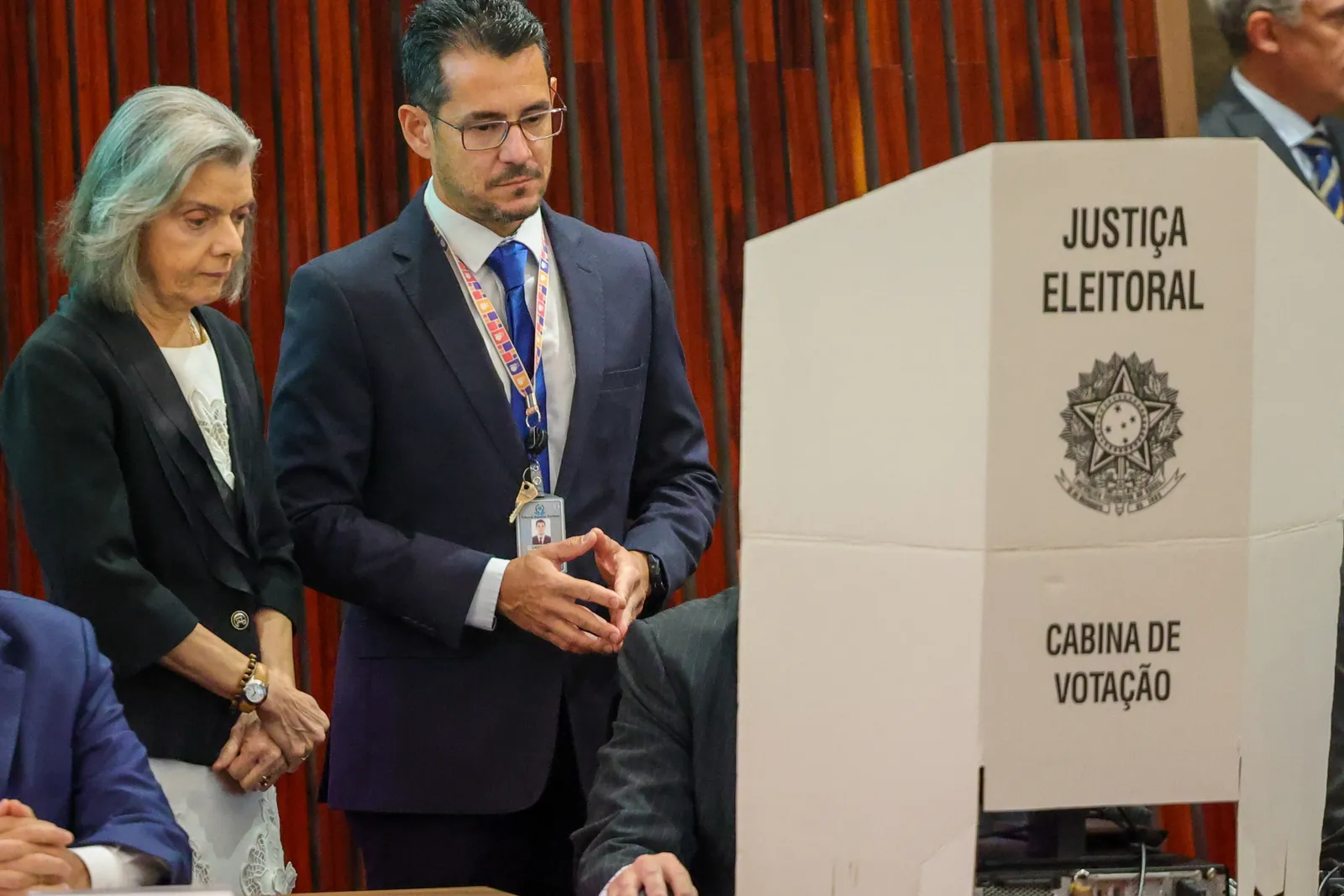 Cabina de votação da Justiça Eleitoral, com o brasão da República, ao lado de autoridades durante cerimônia no Tribunal Superior Eleitoral.