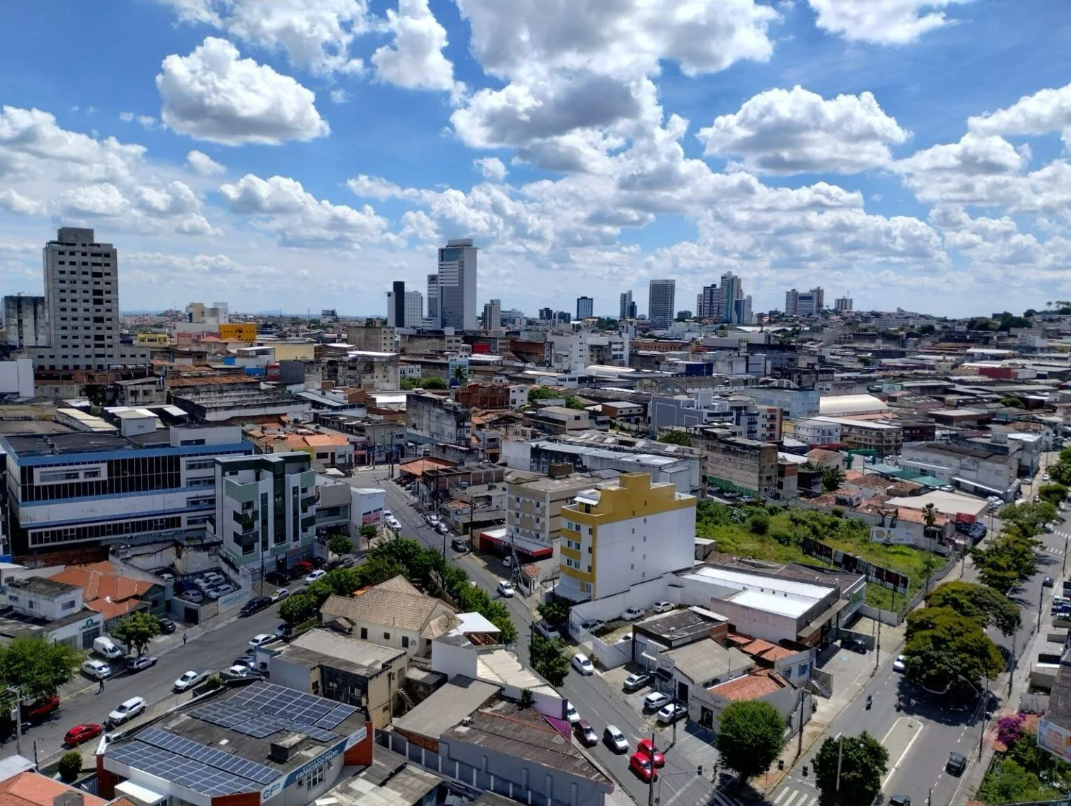 Vista aérea da área central de Campina Grande, com casas, prédios comerciais e torres residenciais ao fundo sob céu de nuvens.