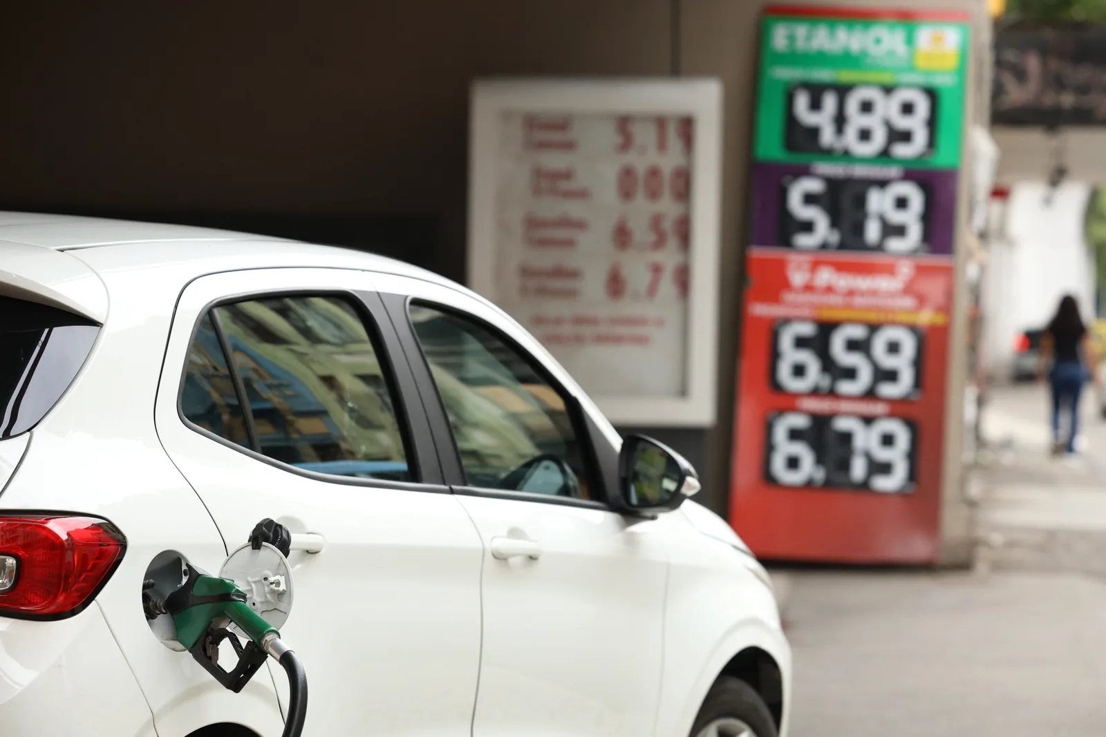 Carro abastece em posto de combustíveis com painel de preços ao fundo