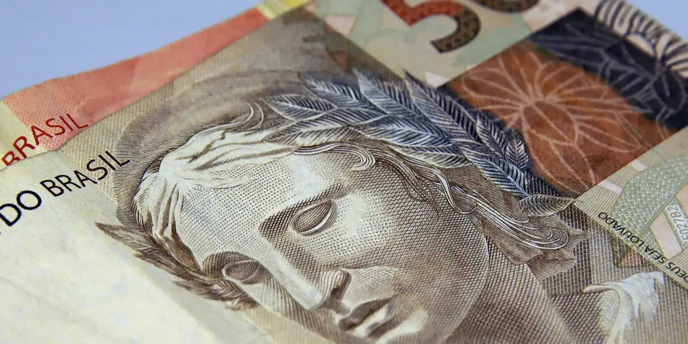 Cédulas de real de diferentes valores dispostas lado a lado, em close, representando dinheiro e poupança.