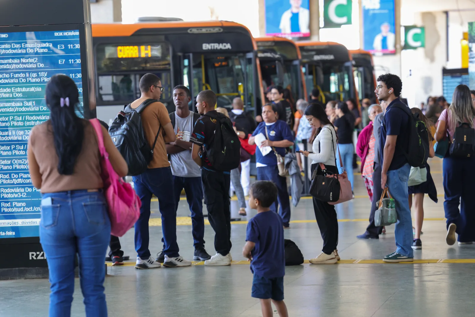 Filas de passageiros e ônibus em uma rodoviária de transporte interestadual.