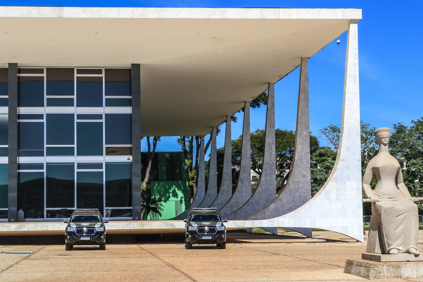 Fachada do edifício-sede do STF, com a escultura A Justiça e viaturas oficiais em frente ao prédio.