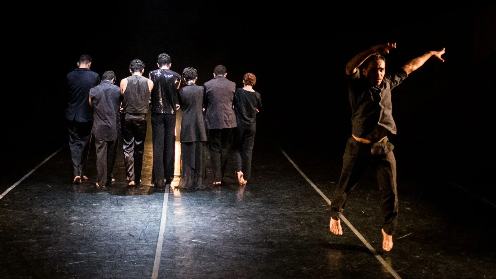 Bailarinos em cena no palco do Teatro Municipal Severino Cabral, com um dançarino saltando à direita e um grupo reunido de costas ao fundo.