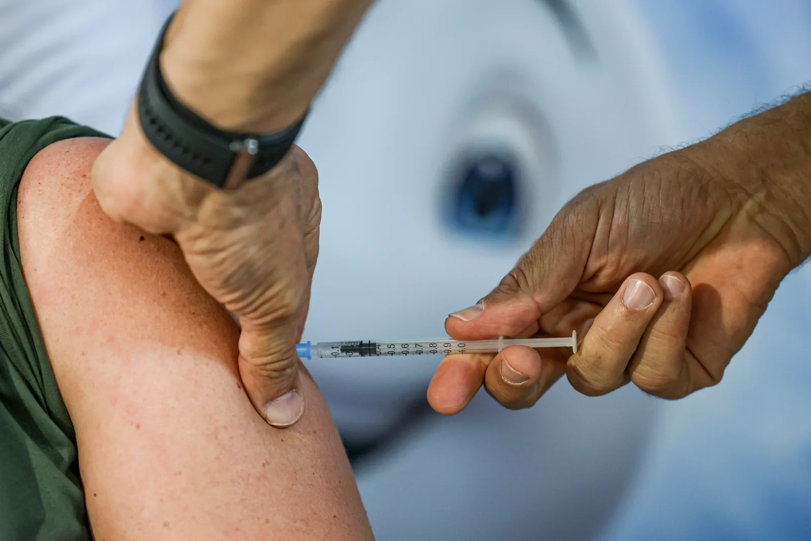 Profissional de saúde aplica uma dose de vacina no braço de uma pessoa, com a seringa em destaque.