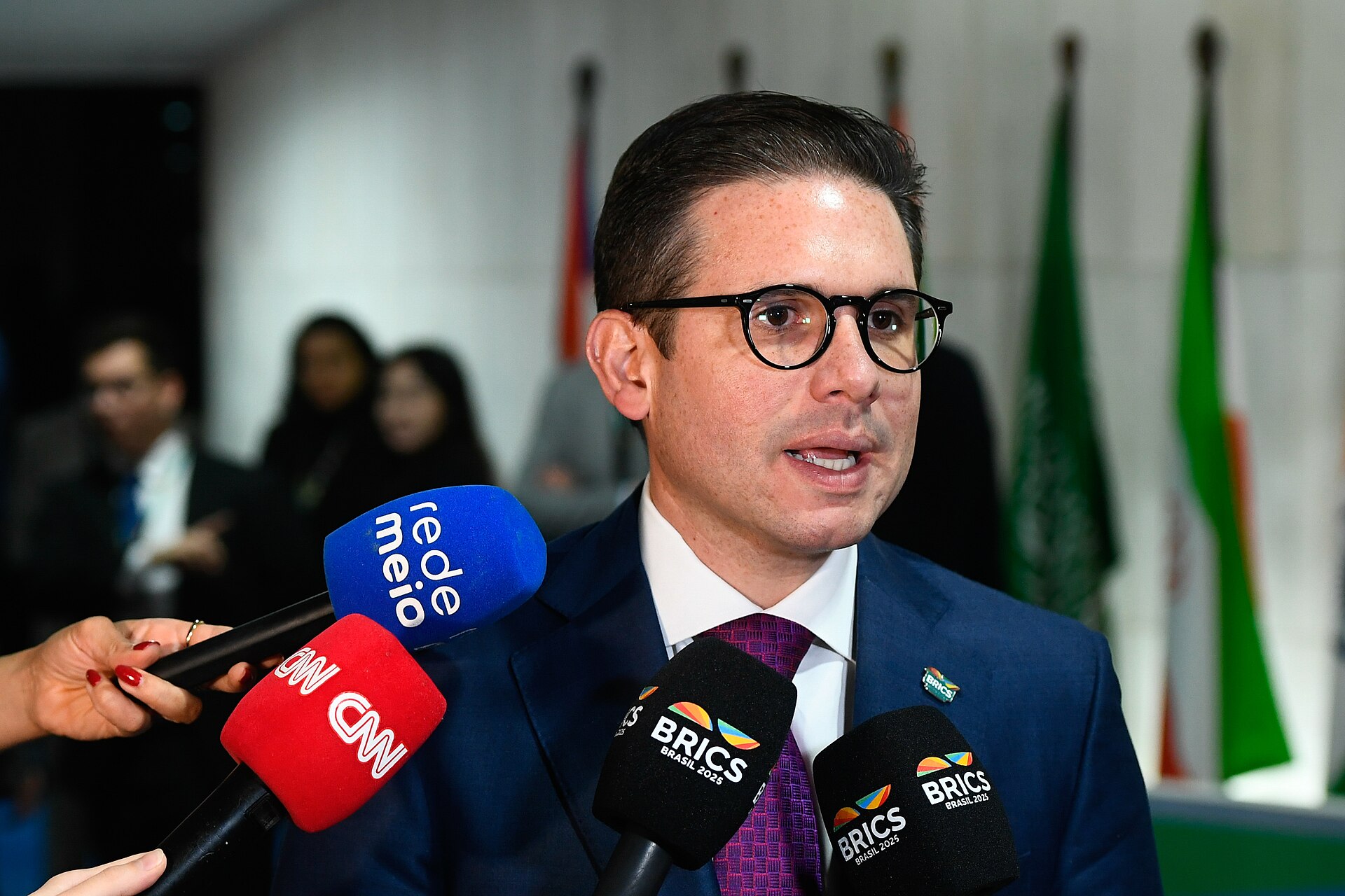 O deputado Hugo Motta, de terno escuro, concede entrevista coletiva em pé diante de microfones.