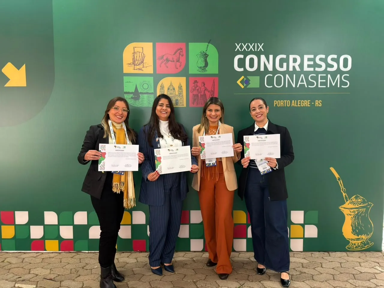 Quatro profissionais de saúde de Campina Grande seguram certificados diante do painel do 39º Congresso do Conasems, em Porto Alegre.