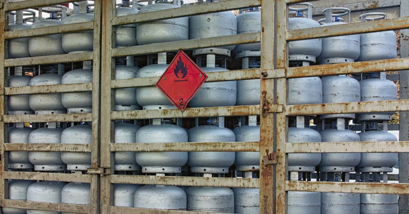 Fileiras de botijões de gás de cozinha de 13 kg empilhados em prateleiras de um caminhão de distribuição, com o símbolo de gás inflamável.